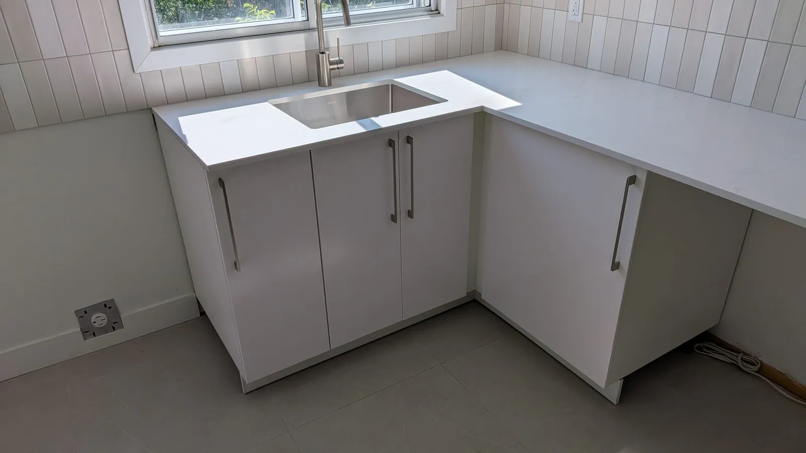 White IKEA SEKTION sink base cabinets with a quartz countertop and tiled backsplash in a Brossard kitchen