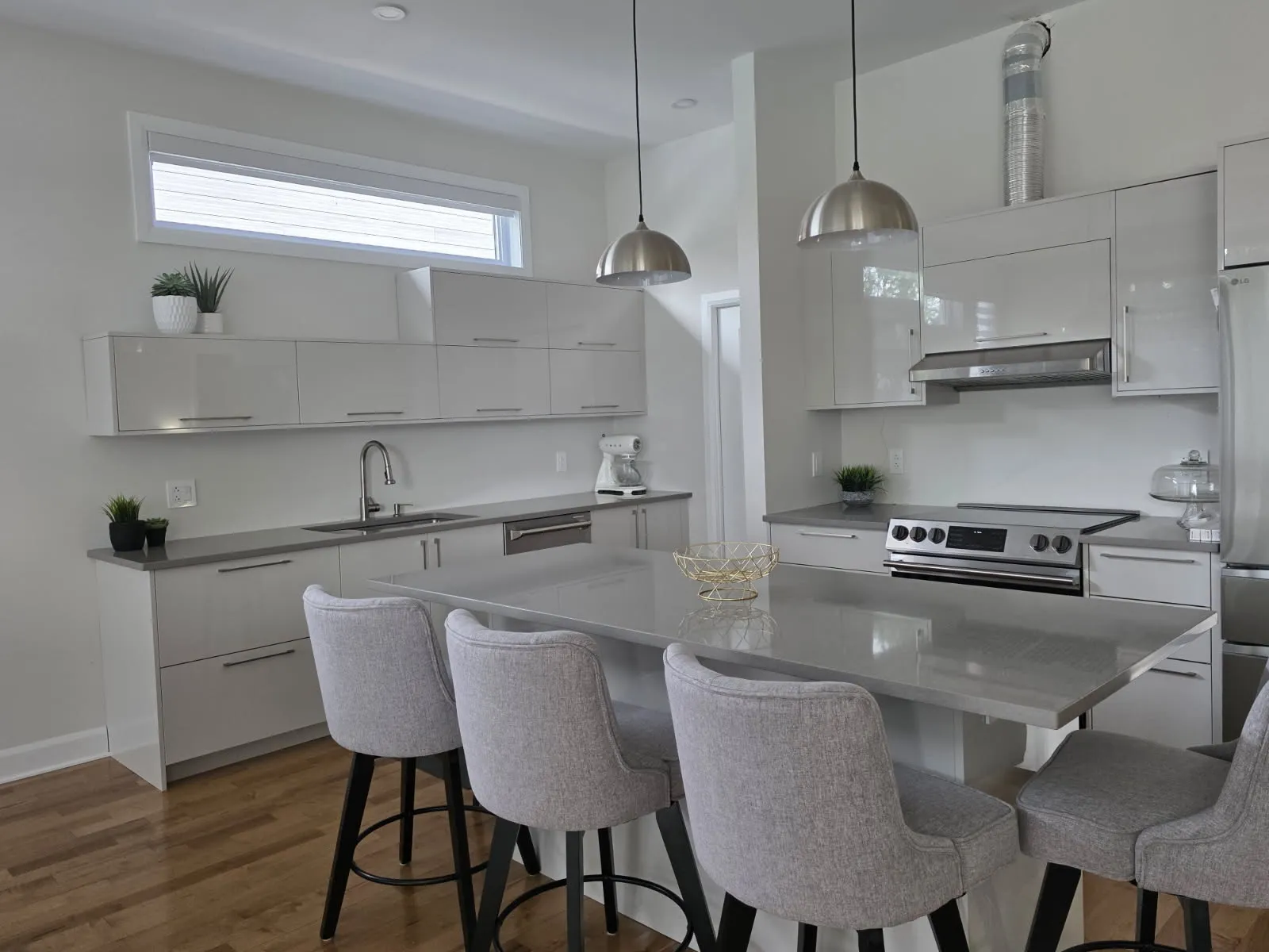 RONA modern white kitchen in Laval with a gray quartz island, four upholstered bar stools and pendant lights