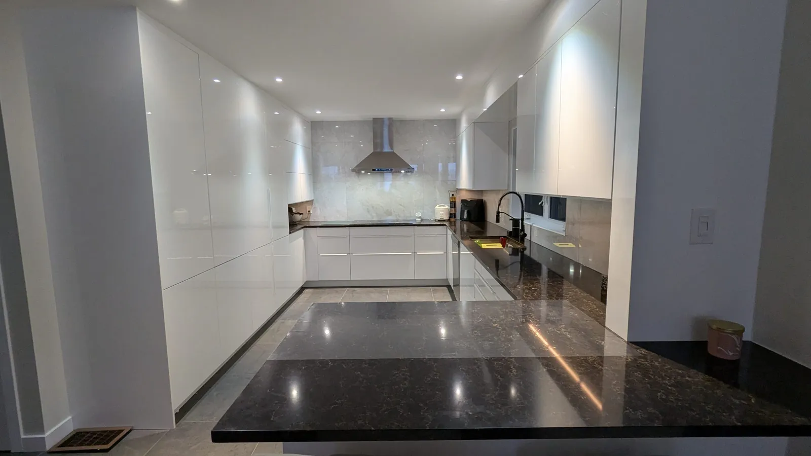 White high-gloss IKEA SEKTION kitchen in Kirkland with tall cabinets, range hood and a dark granite peninsula