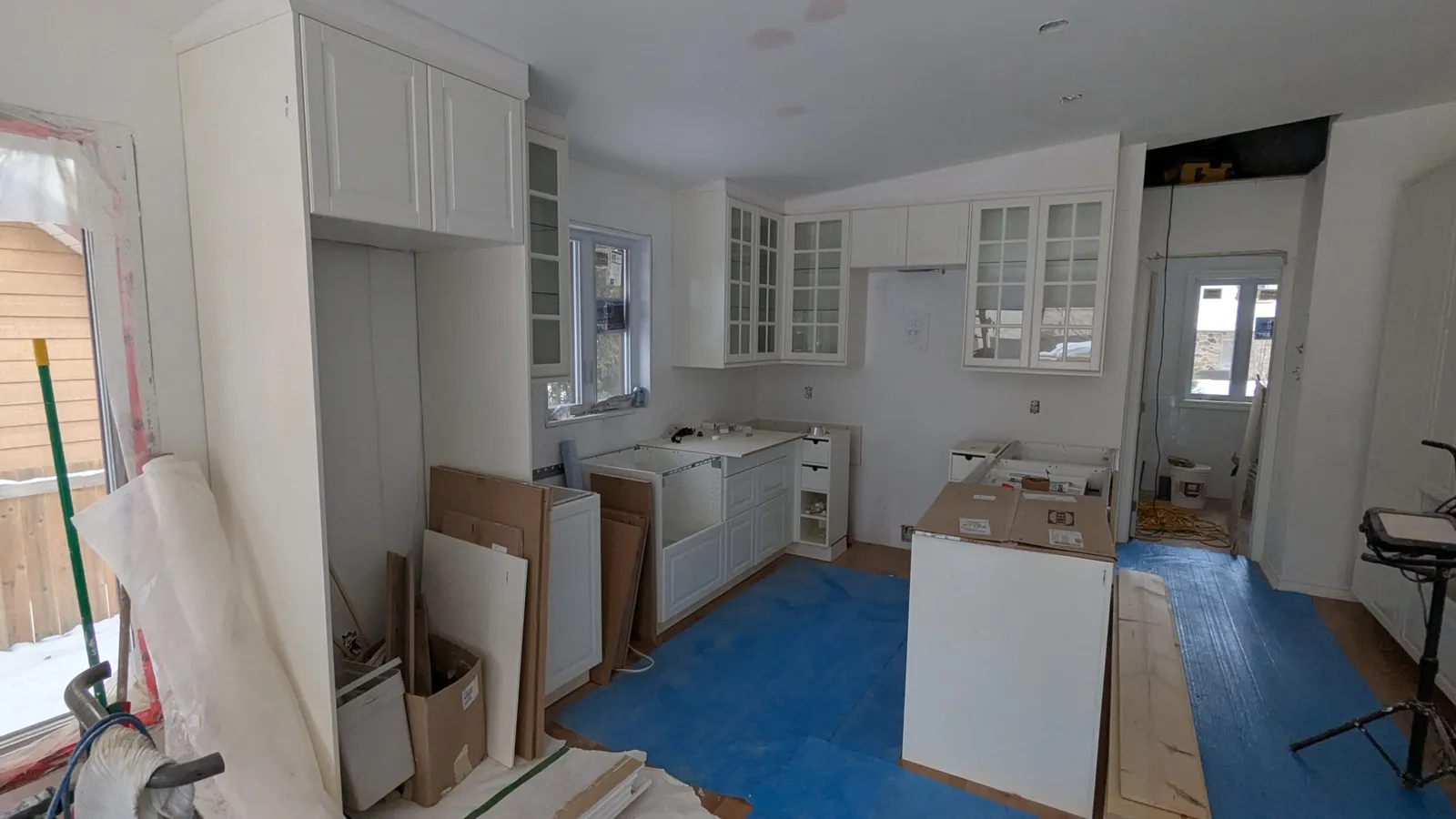 White shaker cabinets with glass doors being installed, floor protected with blue film, Deux-Montagnes