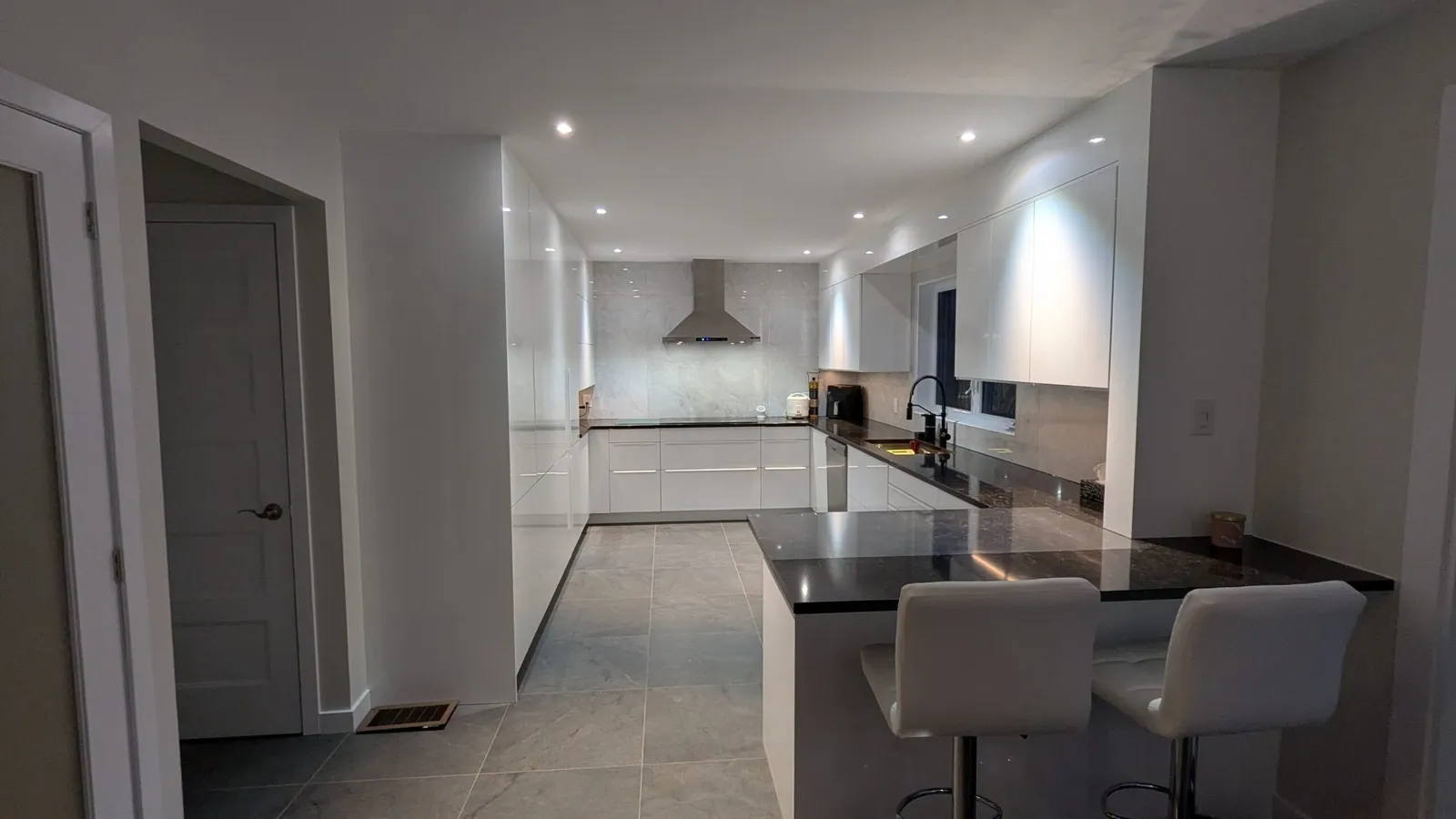Dark granite peninsula with two white bar stools beside high-gloss white cabinets in a Kirkland kitchen
