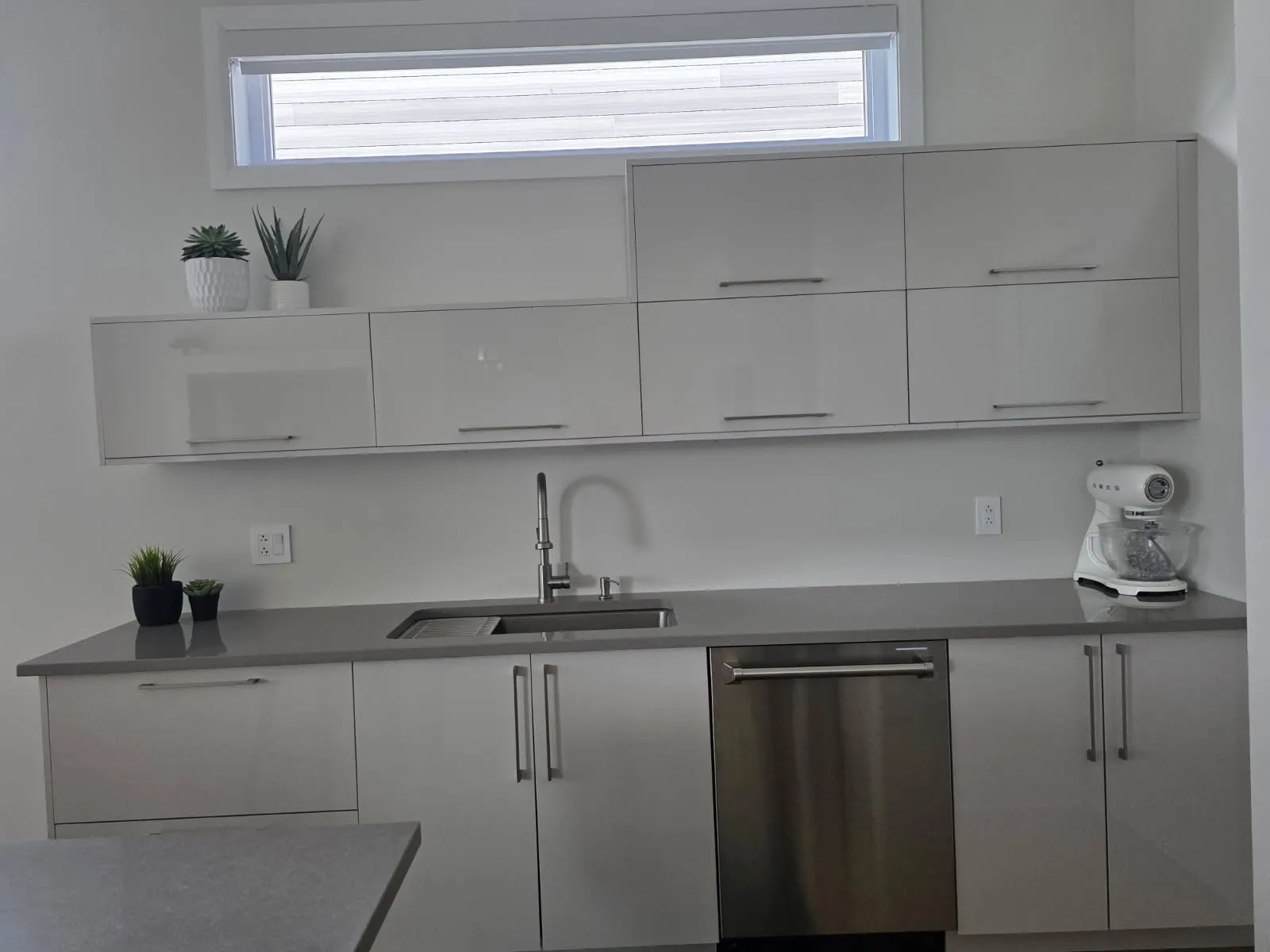 Sink wall of a RONA kitchen in Laval with glossy upper cabinets, gray quartz countertop and stainless dishwasher