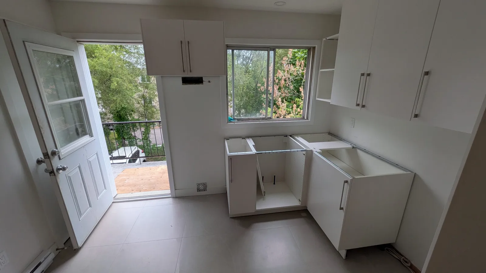 White upper and base cabinets being installed beside a window and balcony door in Brossard