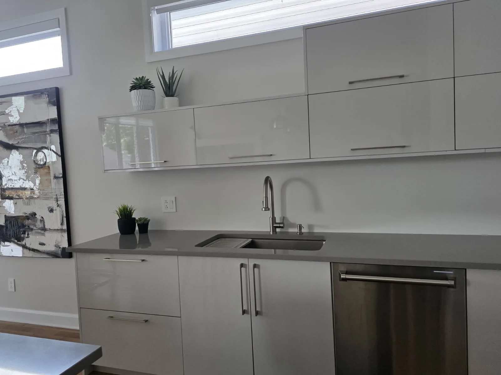 Close view of glossy upper cabinets, undermount sink and gray quartz countertop in a Laval kitchen