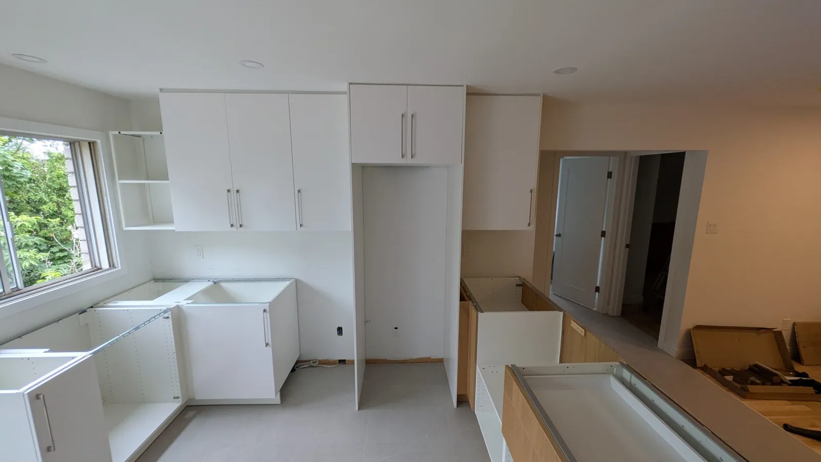 Brossard kitchen installation in progress: white tall and upper cabinets in place, base units being assembled