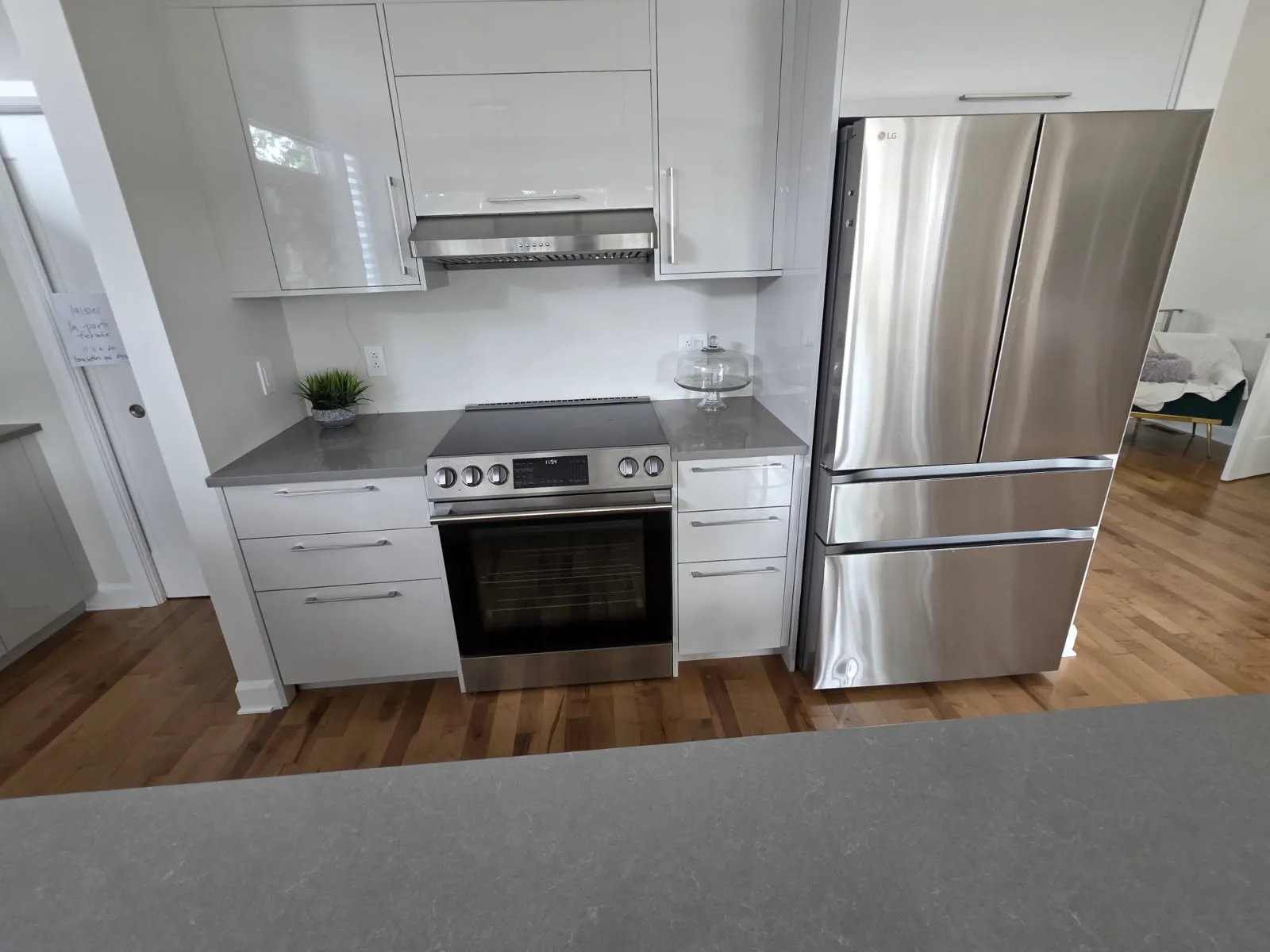 Cooking area with electric range, hood and refrigerator beside light-colored cabinets in a Laval kitchen